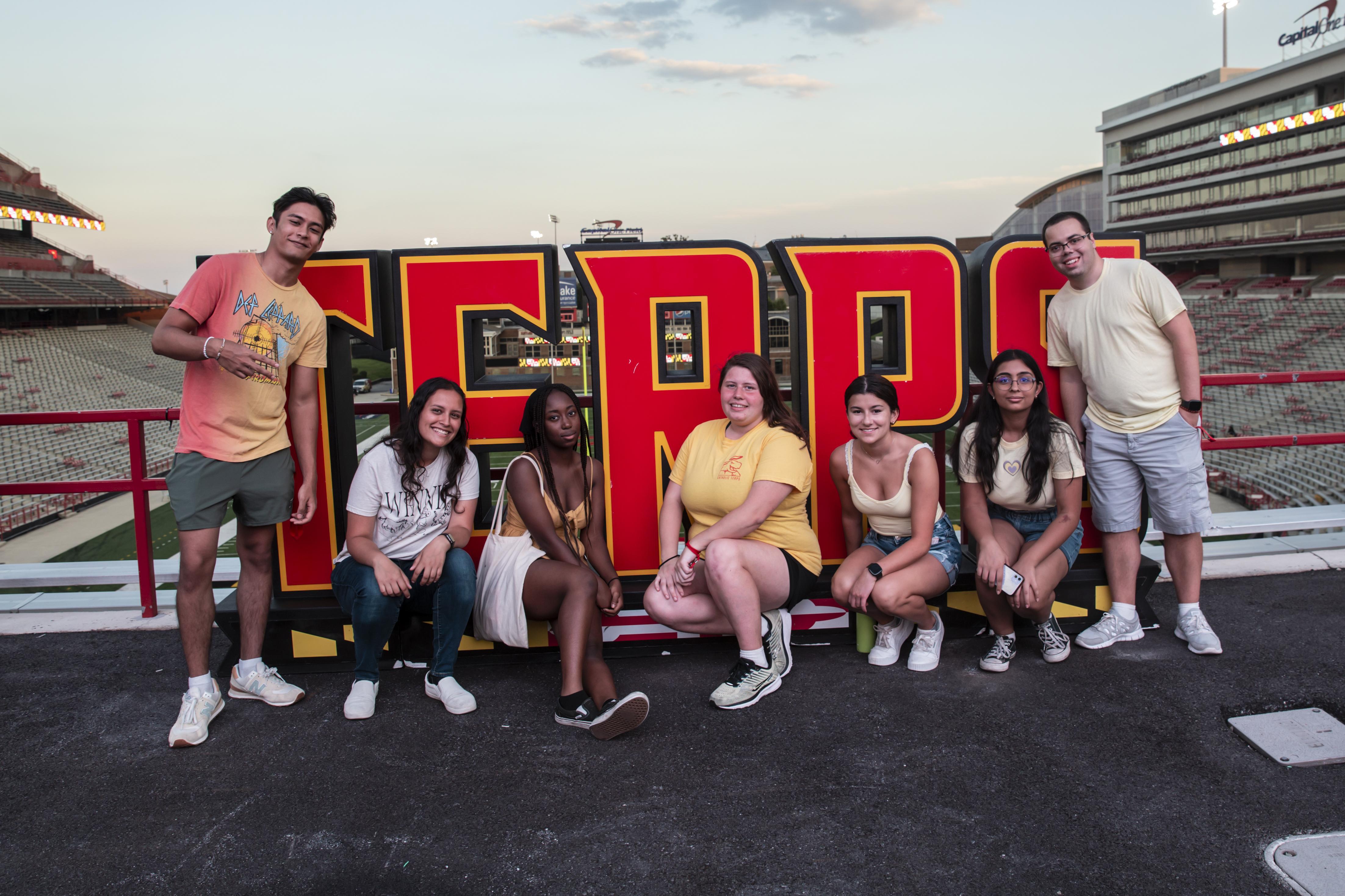 seven students posing with TERPS signage at the Big Show in the football stadium event during Fall Welcome