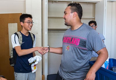 two students shaking hands in dorm room