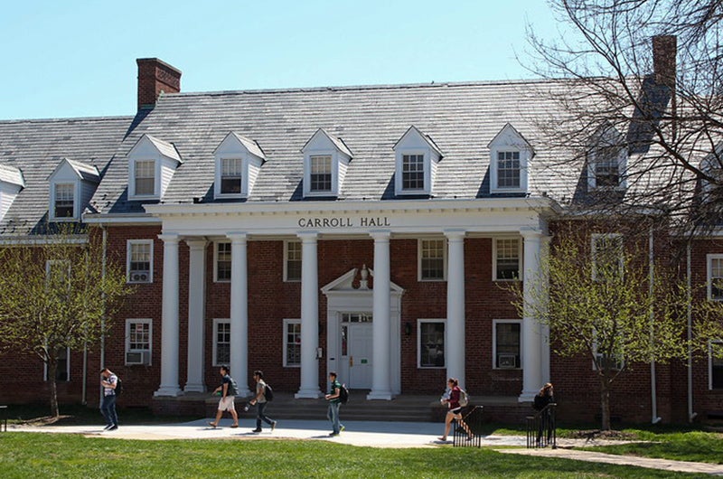 Exterior view of Carroll Hall, a brick building with white columns and students walking in front.