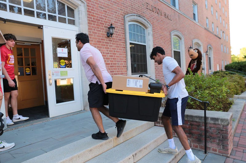 two people carrying a plastic storage plate through the doors of a residence hall during move-in