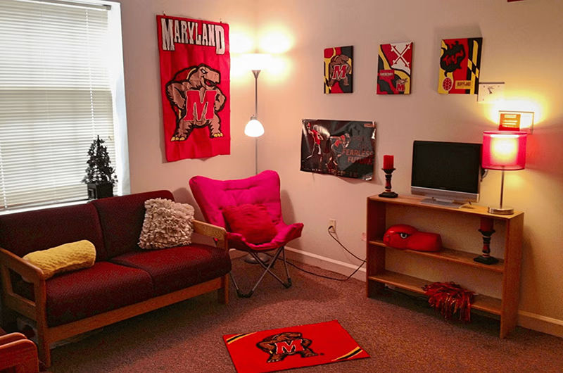 Common space with a red sofa, pink chair, and Maryland Terrapins posters and rug.