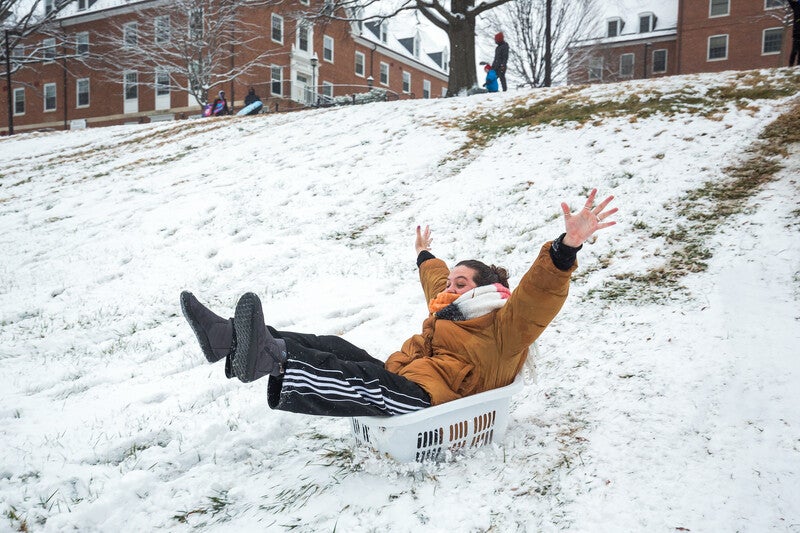 student sliding down snowy hill in laundry basket