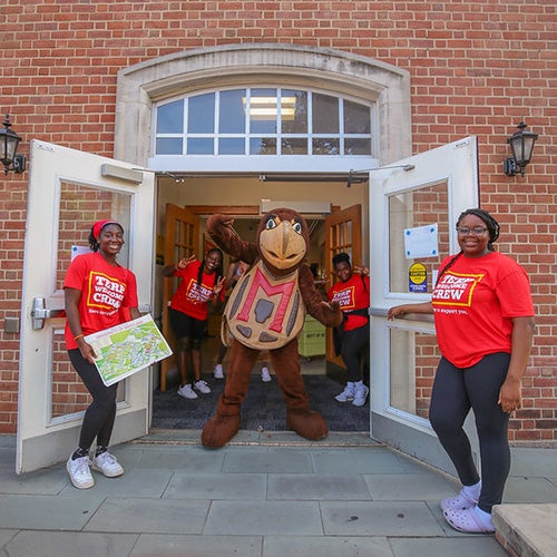 Students wearing red "Terp Welcome Crew" shirts with Testudo posing in a brick doorway.