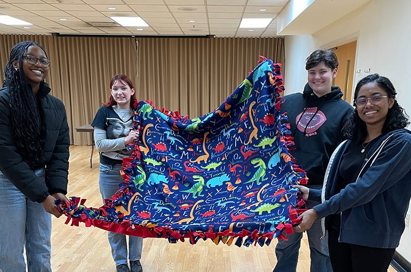 Four students holding up a blanket they made during a Winter Welcome event.