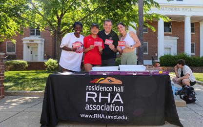 Four people smiling at a Residence Hall Association tabling event on Washington Quad.