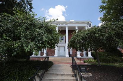 Fraternity house number five, featuring a white columned porch framed by green trees.