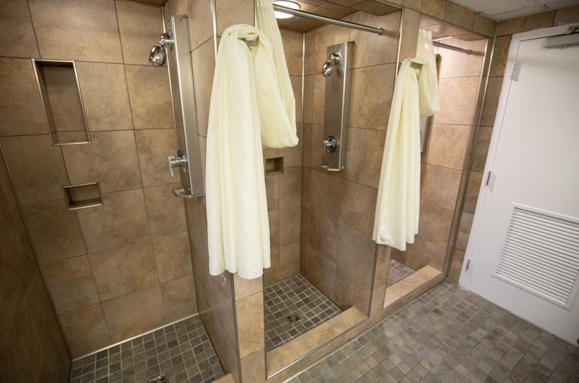Row of tiled shower stalls with curtains in a shared house bathroom.
