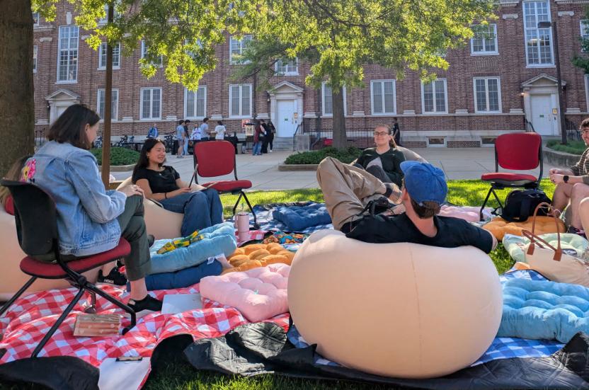 Volunteers sitting on chairs and bean bags and engaging in conversations in a restorative circle outdoors in grassy area outside Calvert Hall in the South Hill community.