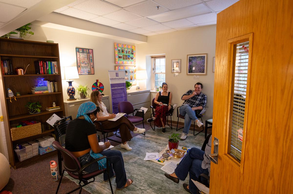 four Resident Life staff members sit in a circular chair arrangement sharing a laugh at the Restorative Circle Center Open House.