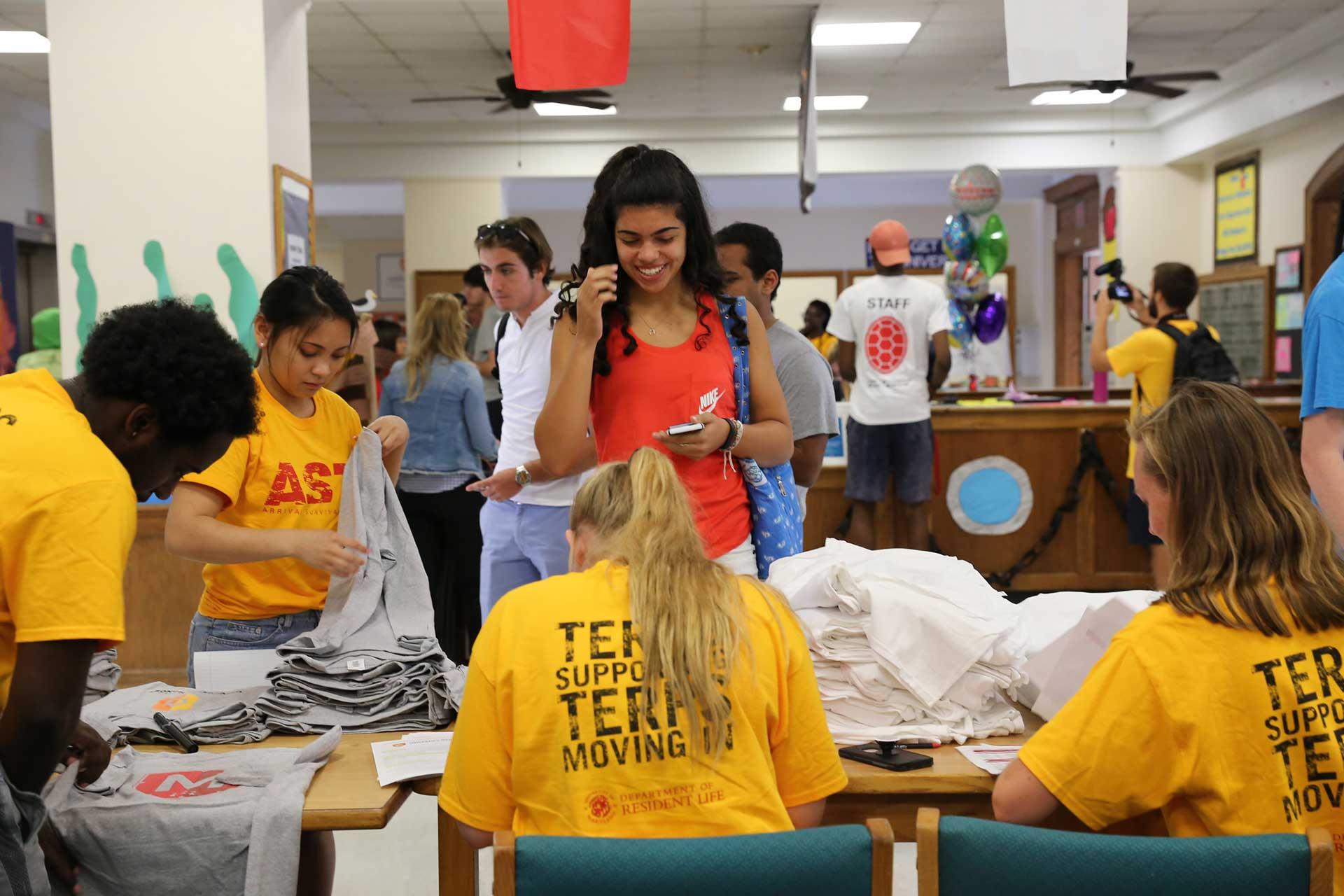 student checking in at desk with t-shirts during fall move in day
