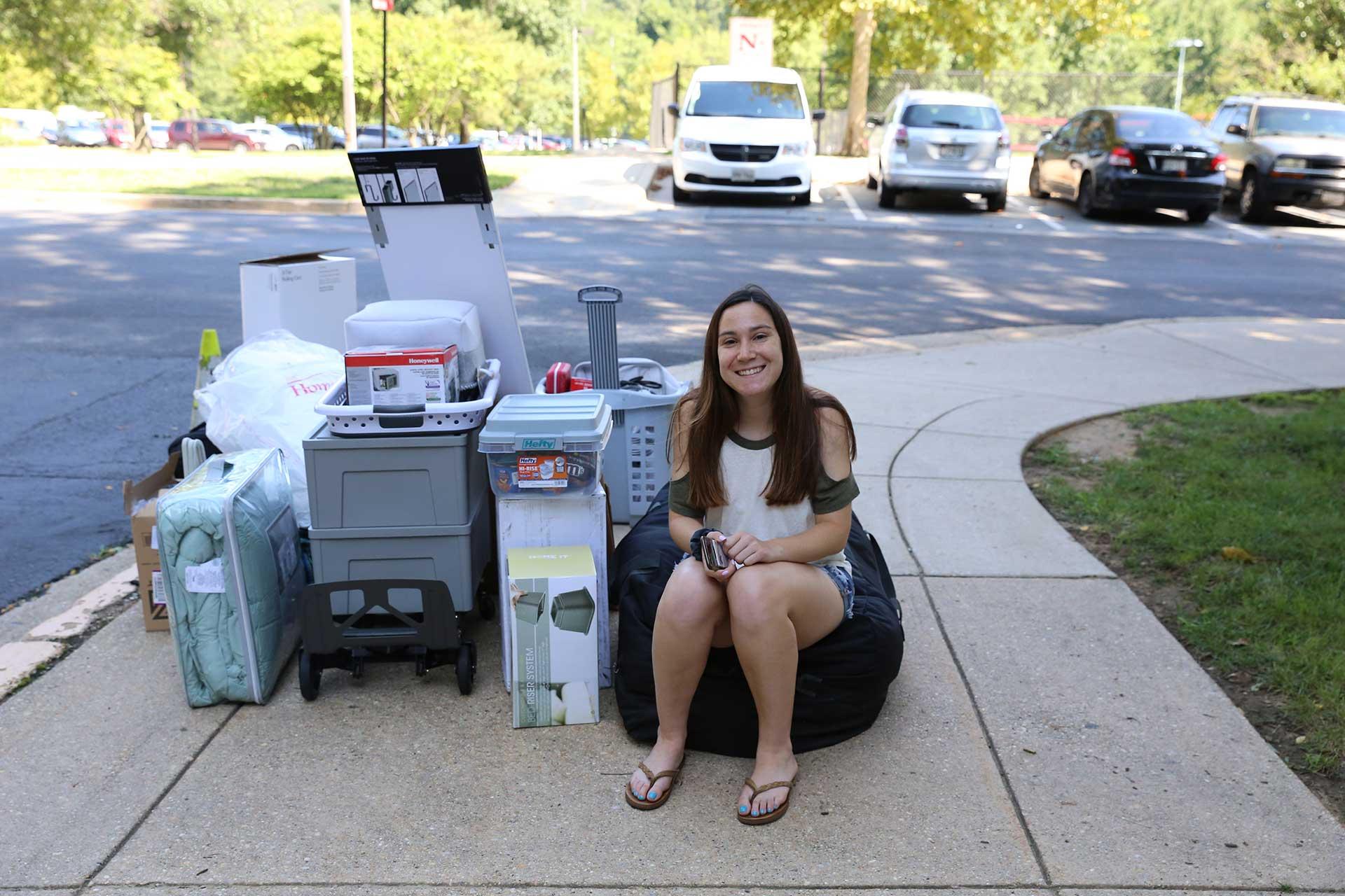 student sitting on the curb with personal items on move in day