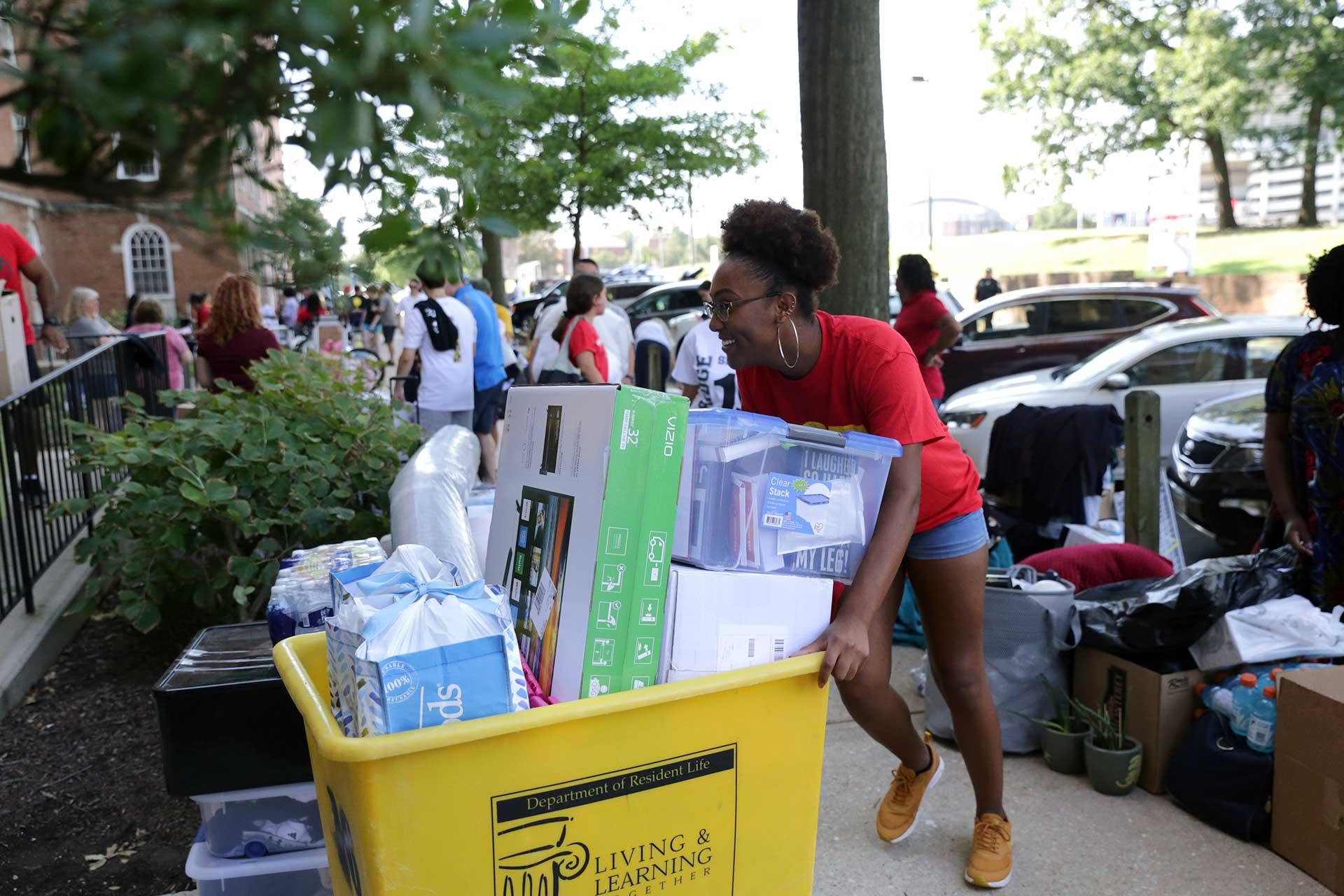 student pushing a moving cart outside a residence hall