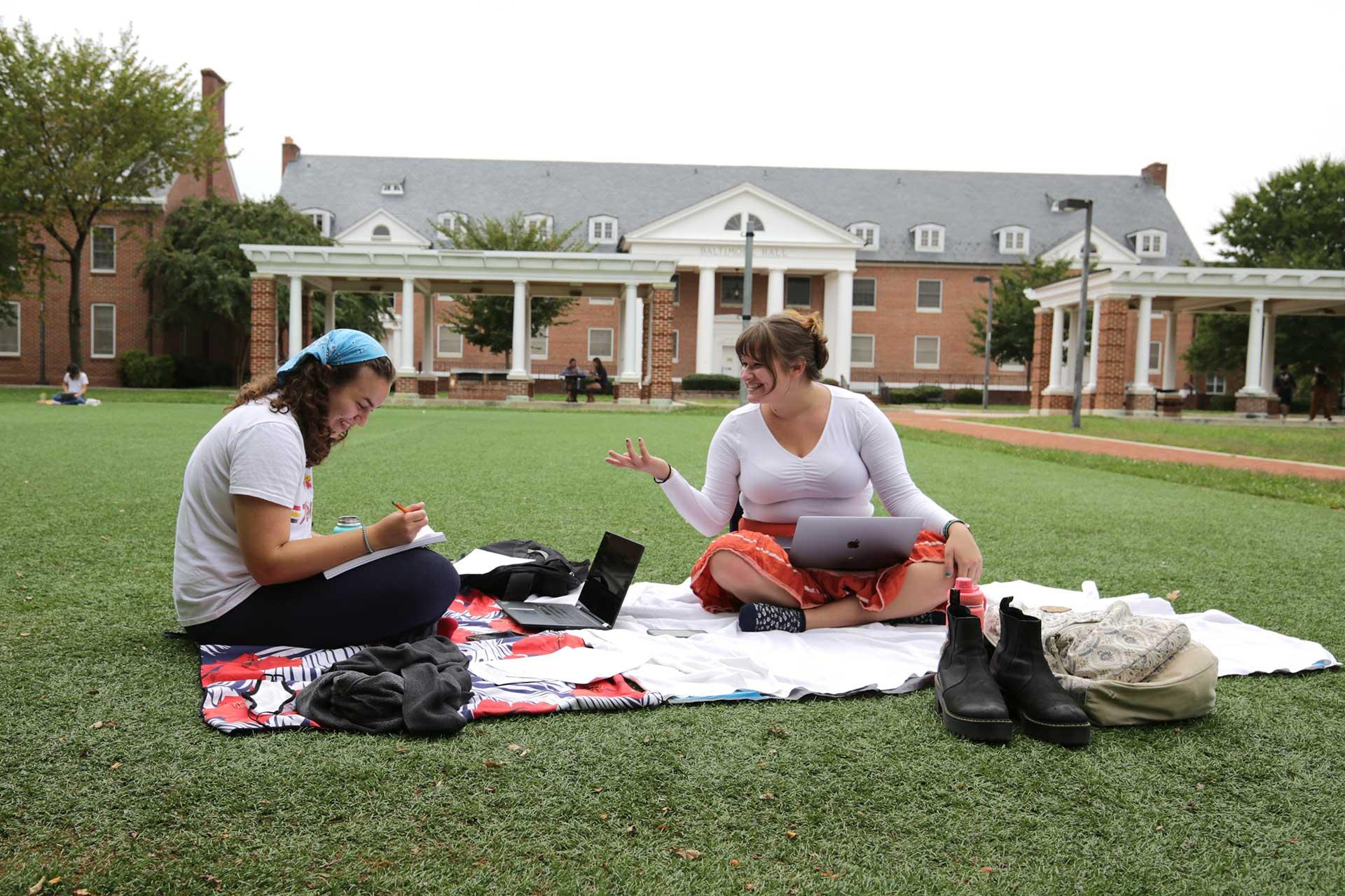 two students sitting on a blanket on the grass
