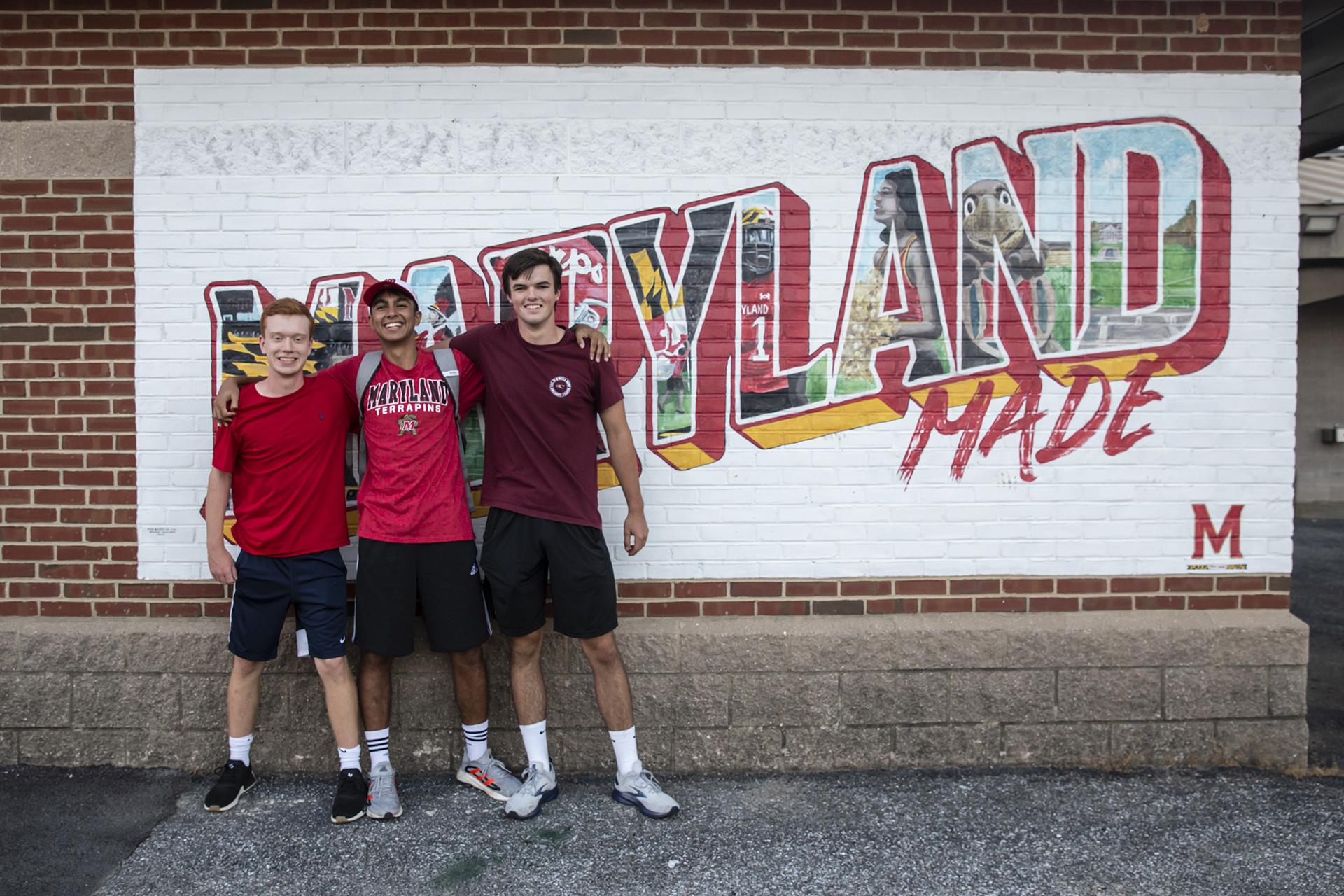 three students posing in front of Maryland Made mural in the football stadium