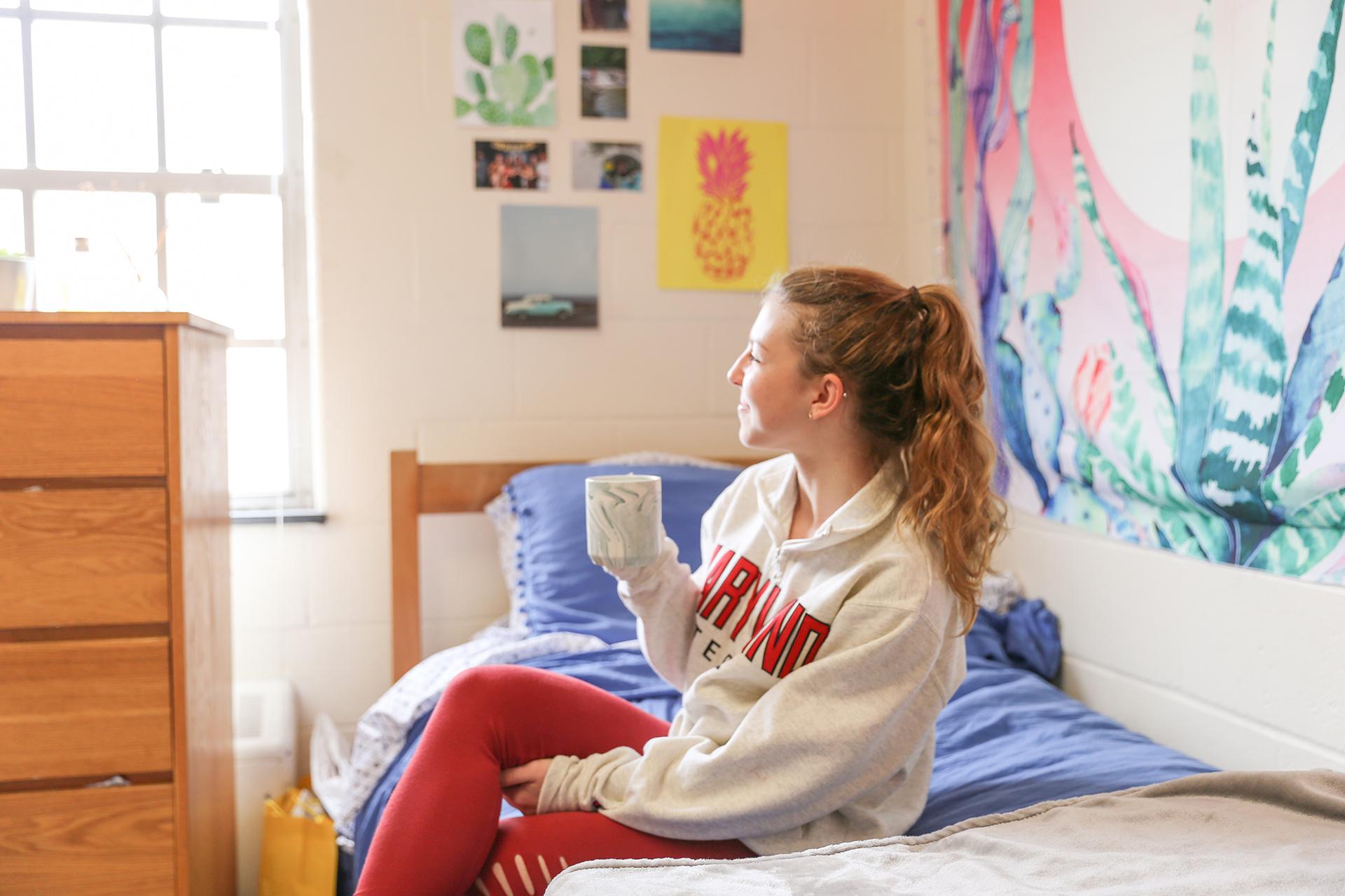 student holding coffee mug sitting in bed and turned sideways