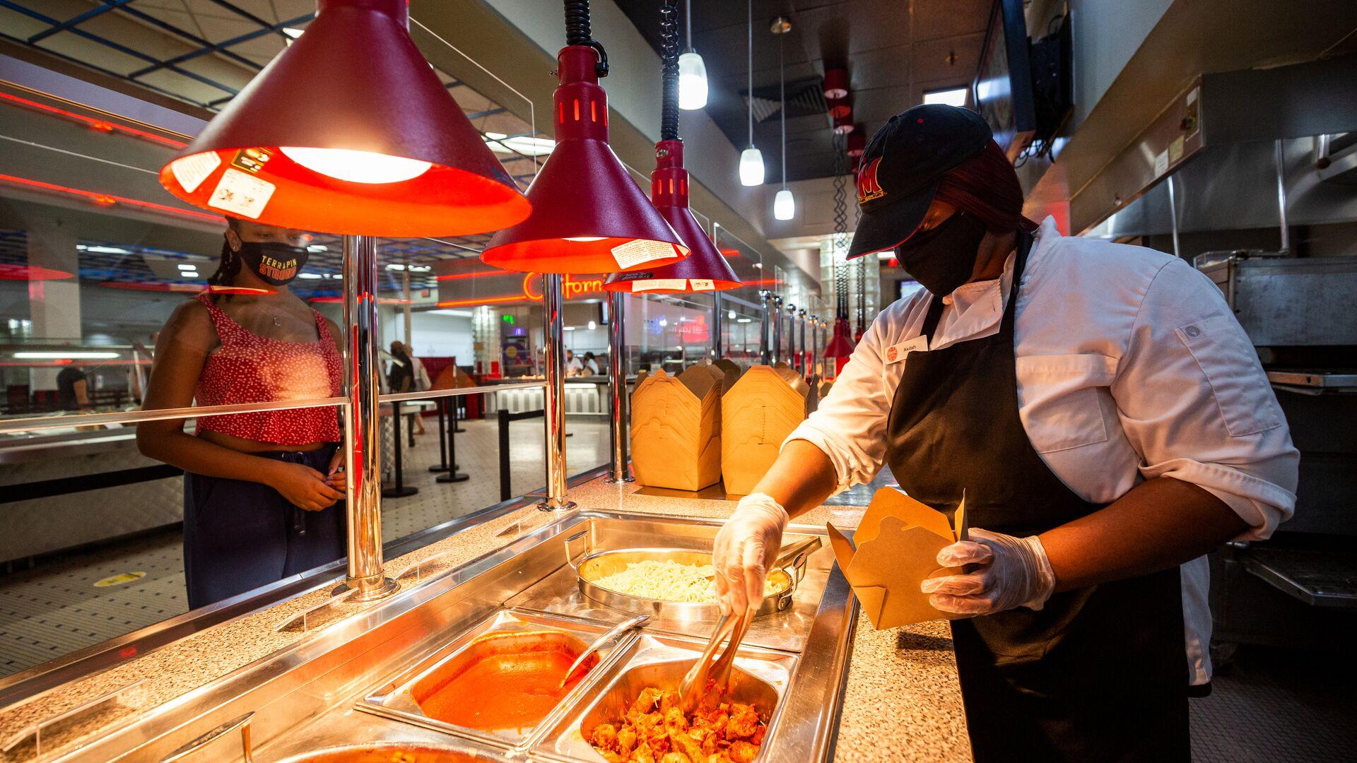 Dining staff member putting pasta in a container in one of the food stations at the Diner as a student waits in line
