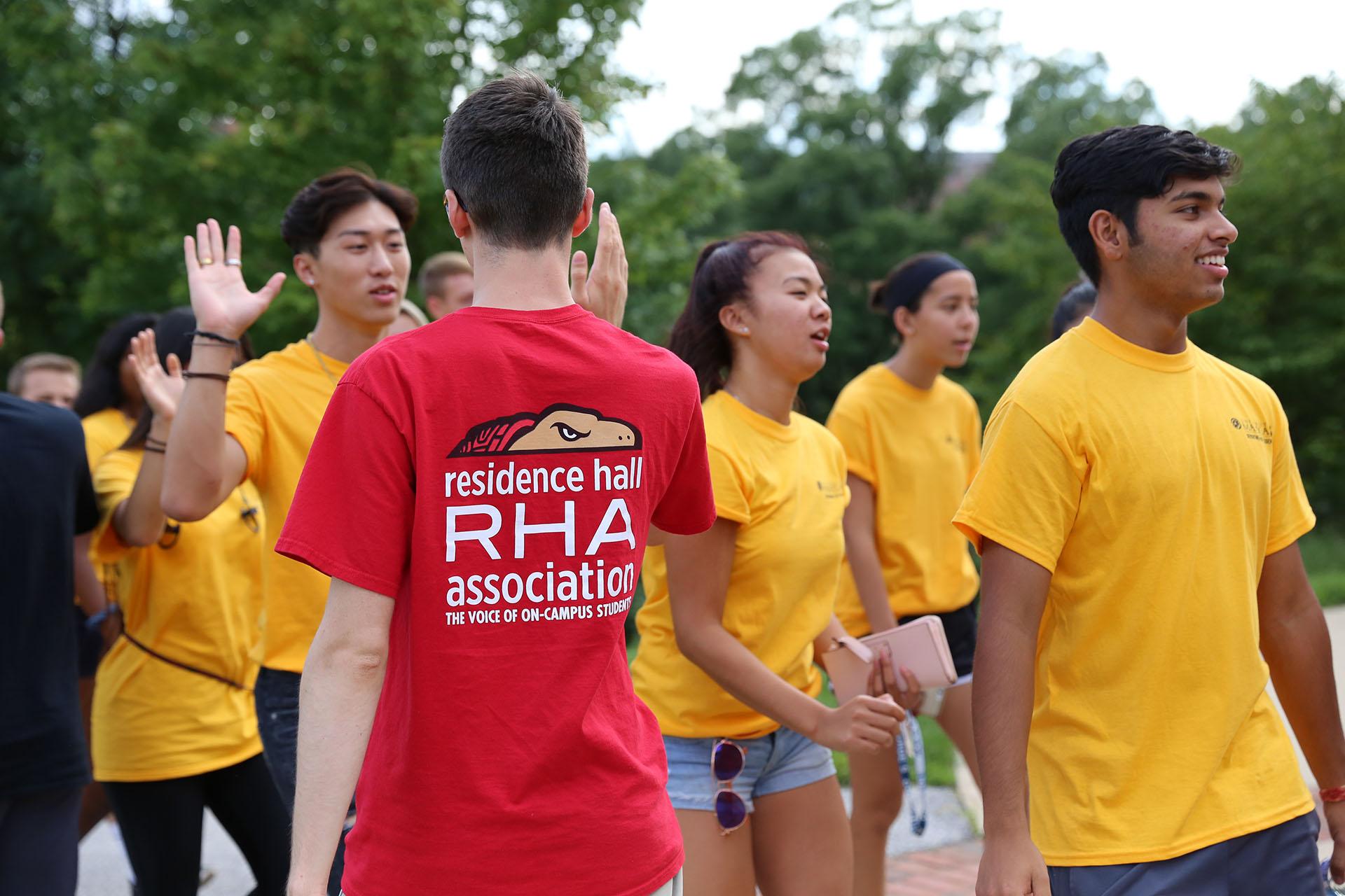 student wearing red RHA shirt high-fiving other students coming towards him in opposite direction with yellow shirts