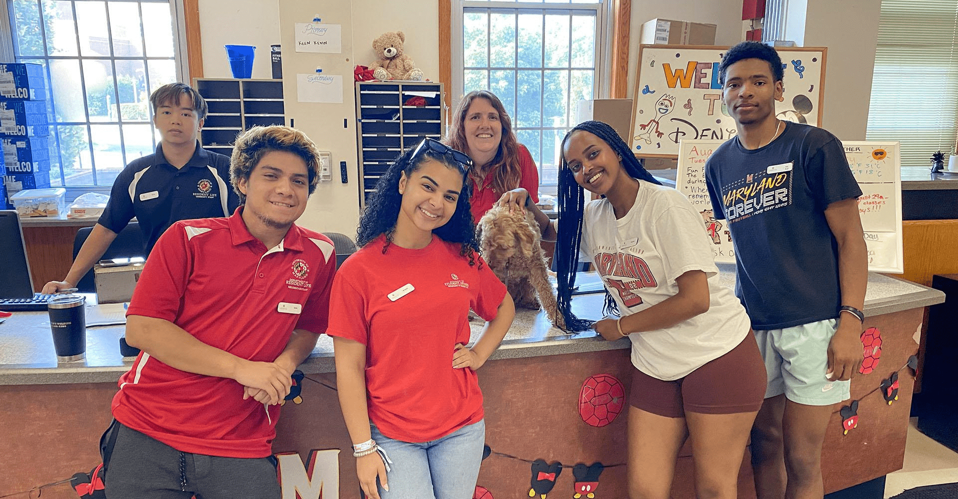 group of resident assistants and resident director posing at a service desk with a dog on the counter