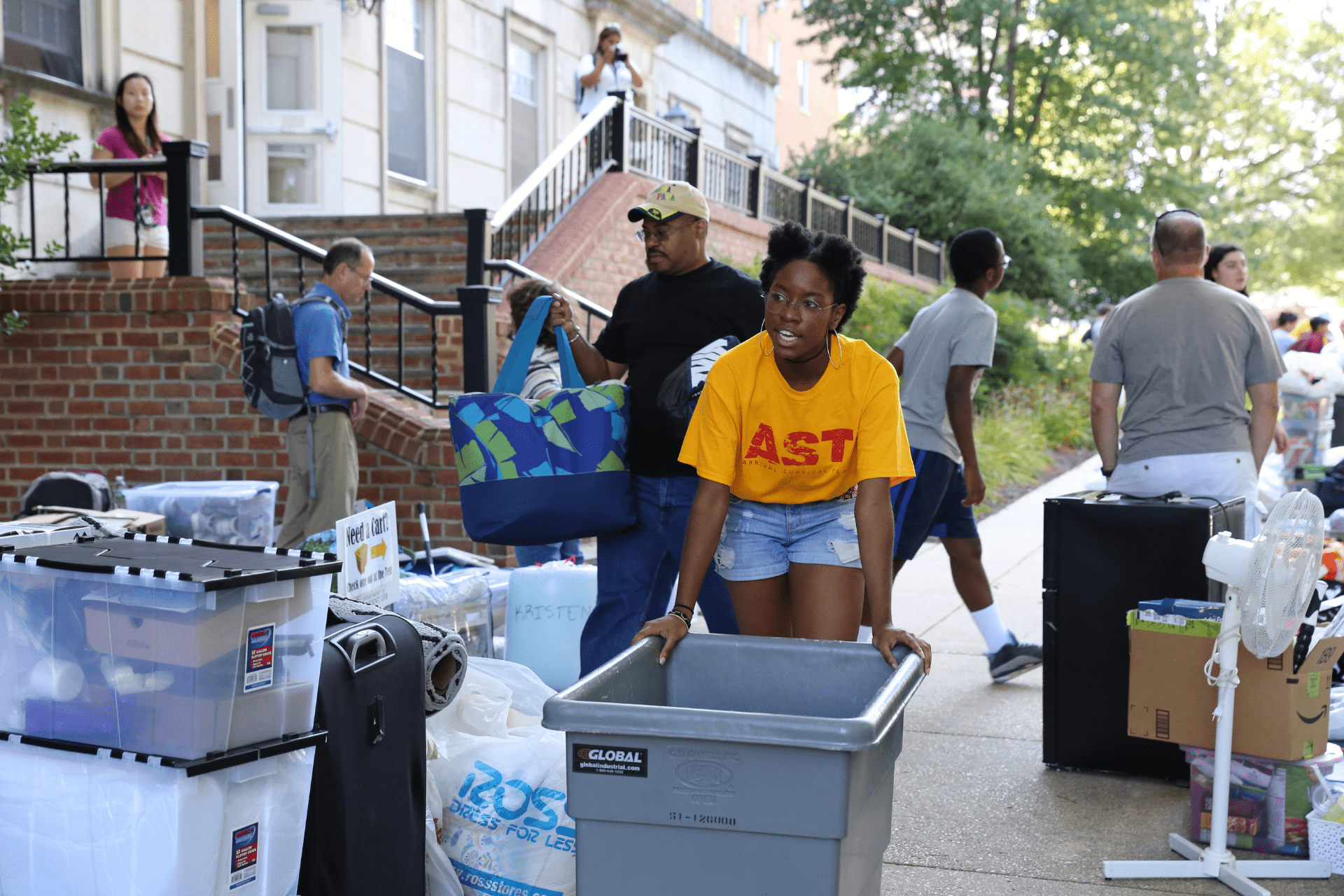 student wearing yellow AST shirt pushing a cart on the sidewalk during move-in
