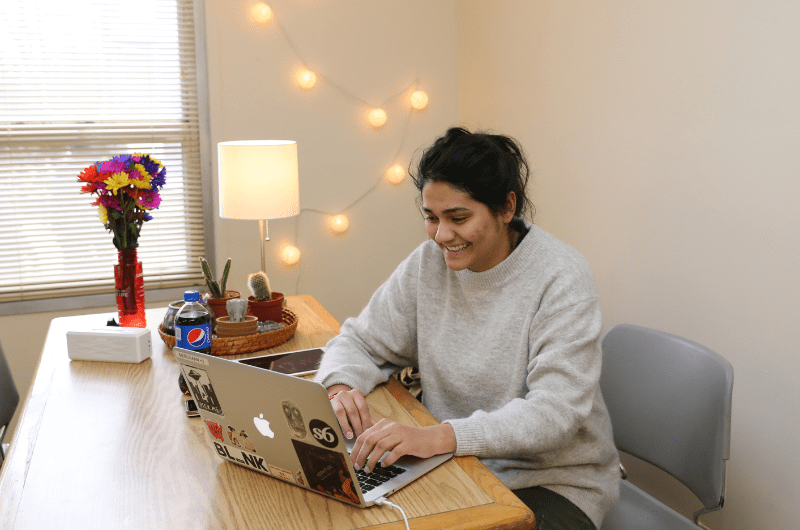 girl smiling while sitting at a table and using her laptop