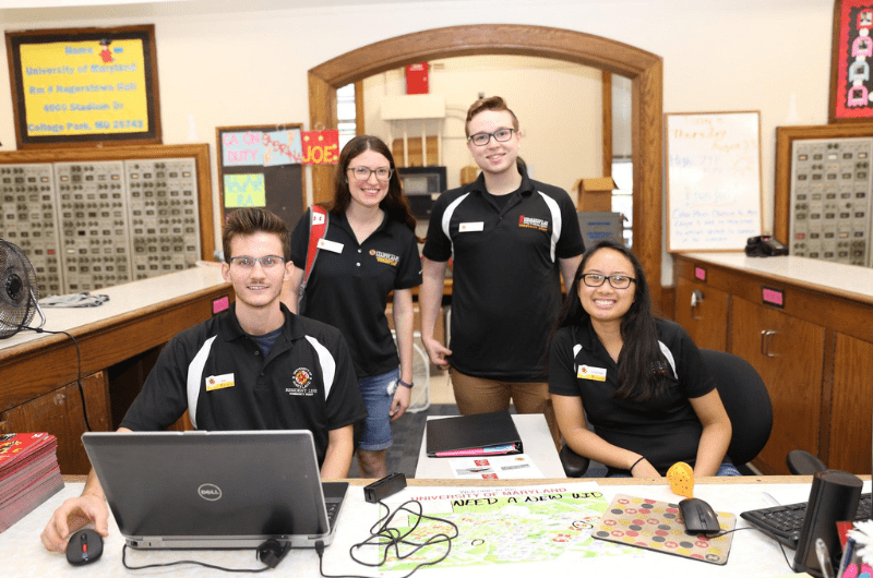 students posing behind a service desk inside a residence hall