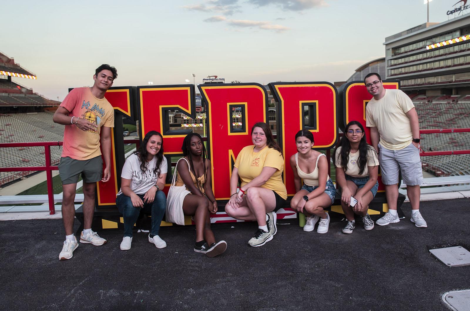 seven students posing with large TERPS sign in the football stadium at sunset