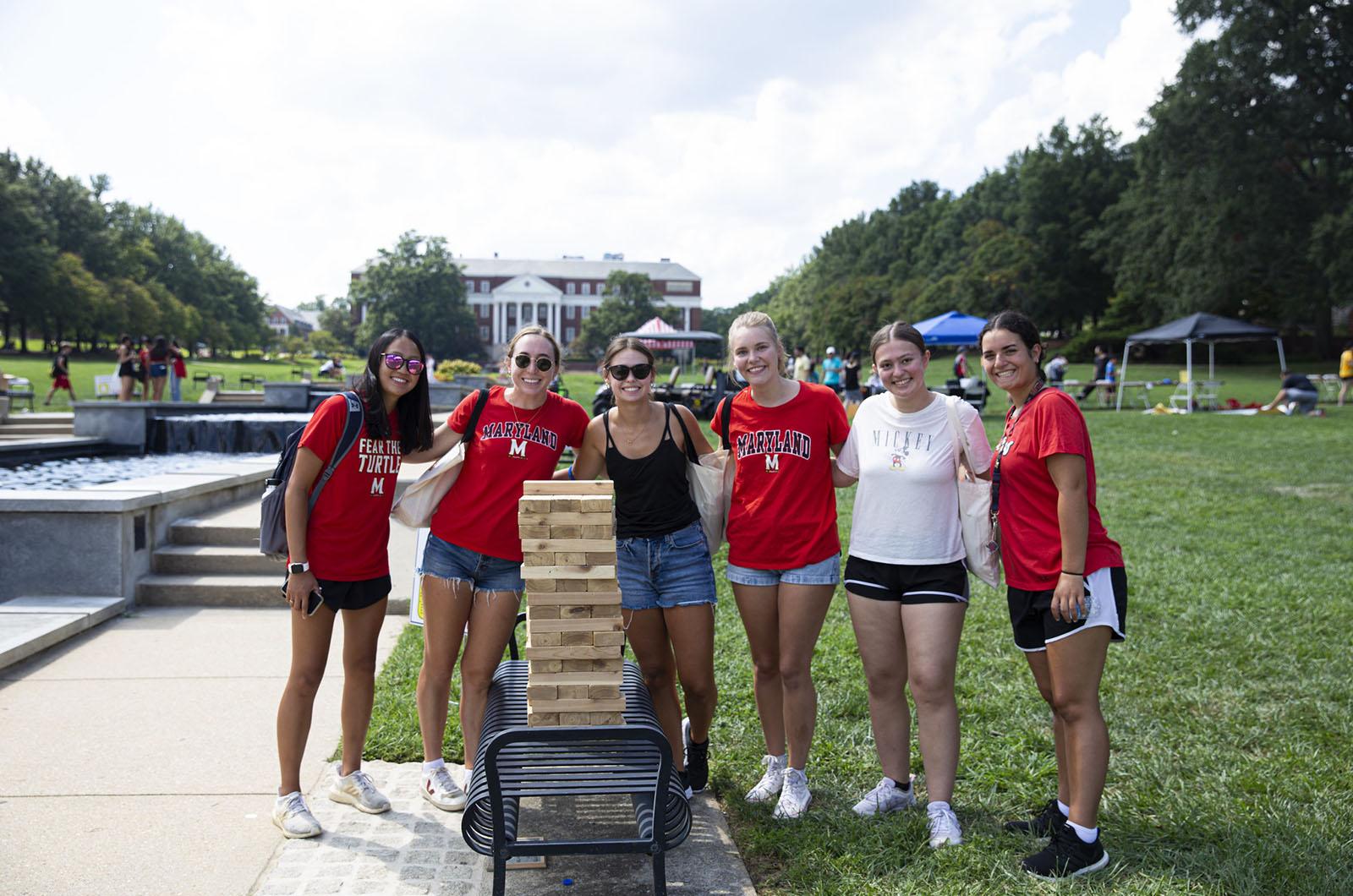 six students posing on McKeldin Mall during Free Fest with a game of giant Jenga in front