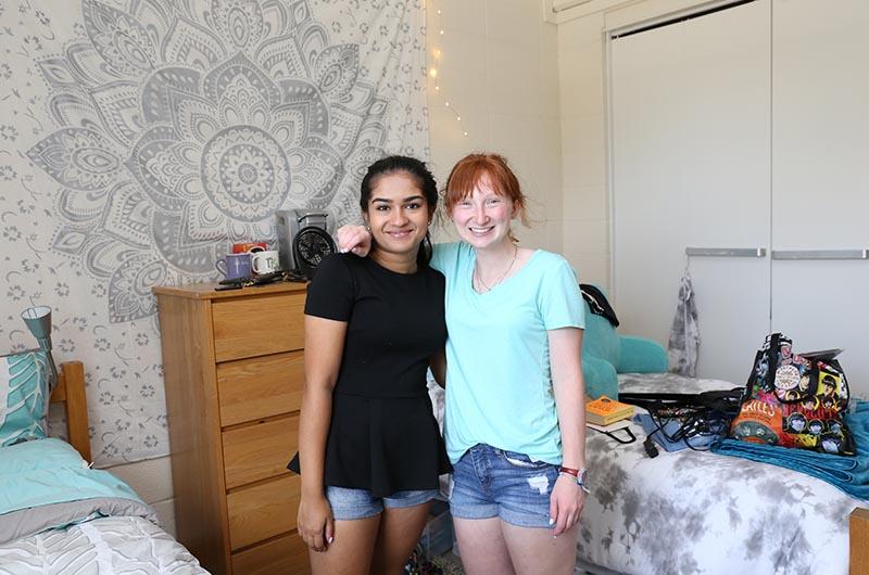 two students standing in between two beds and posing in a residence hall room
