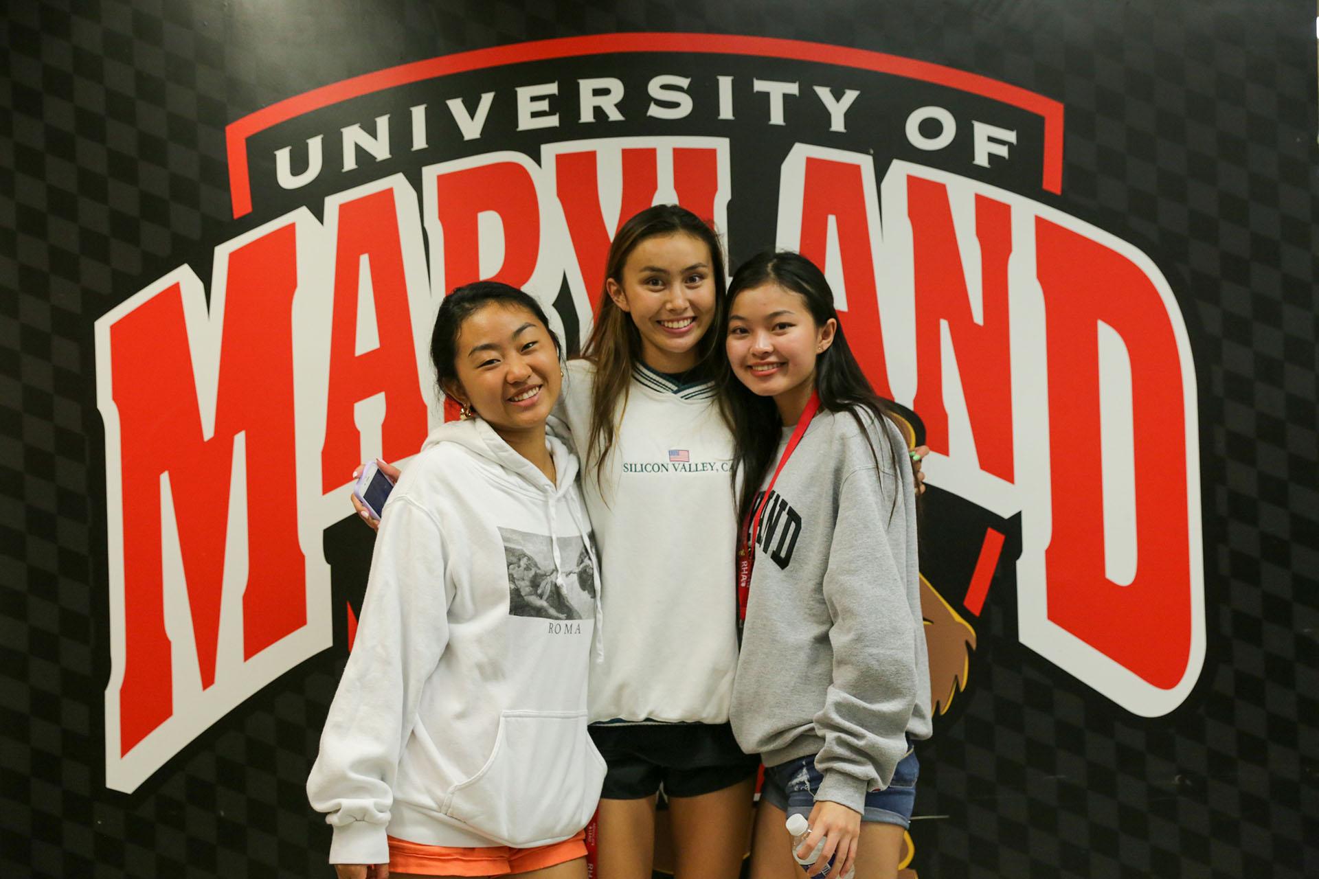 three students posing in front of wall that says University of Maryland