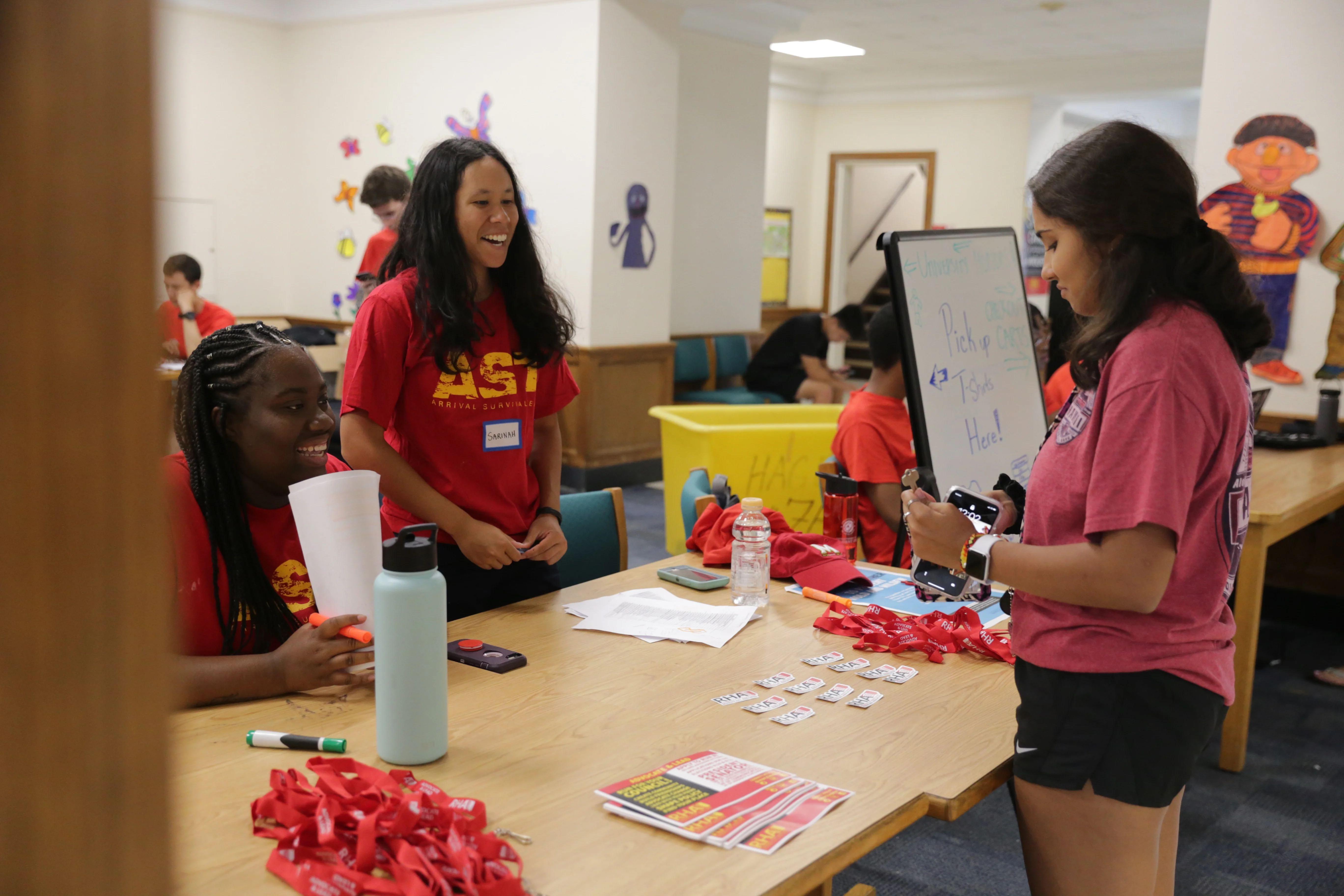 student welcome volunteers at a desk at the entrance of a residence hall helping a student check-in