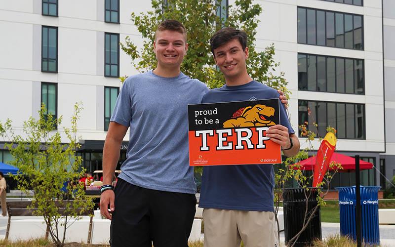 two students holding proud terp sign outside Heritage Plaza during move-in