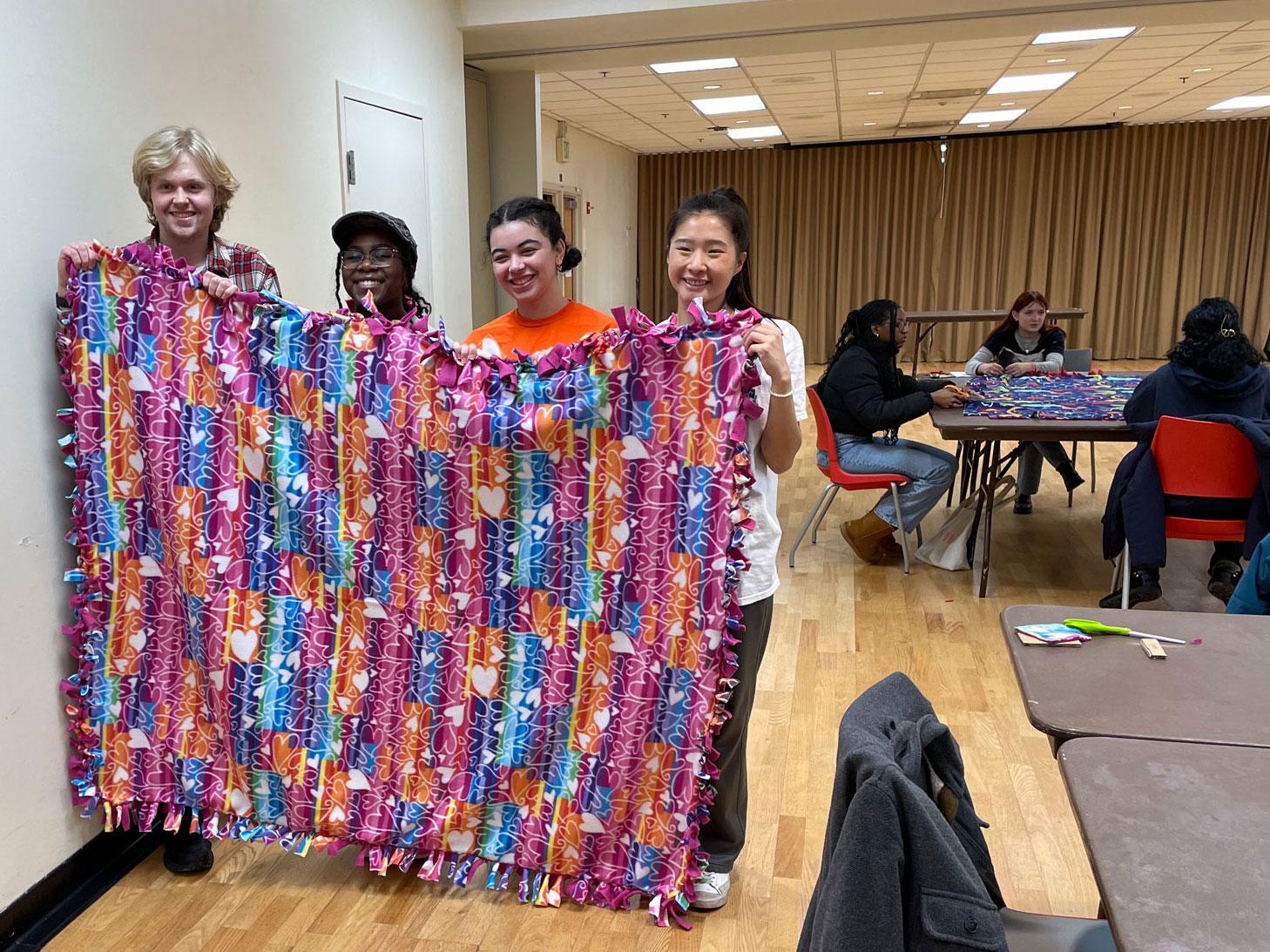 four students holding up quilt they made during a winter welcome event