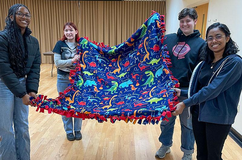 four students holding up a handmade quilt during a Winter Welcome event