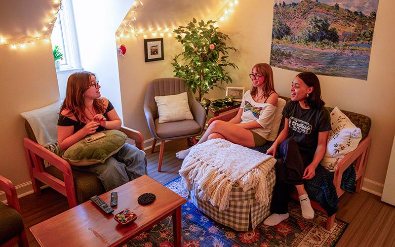 three students in living room in residence hall on south campus