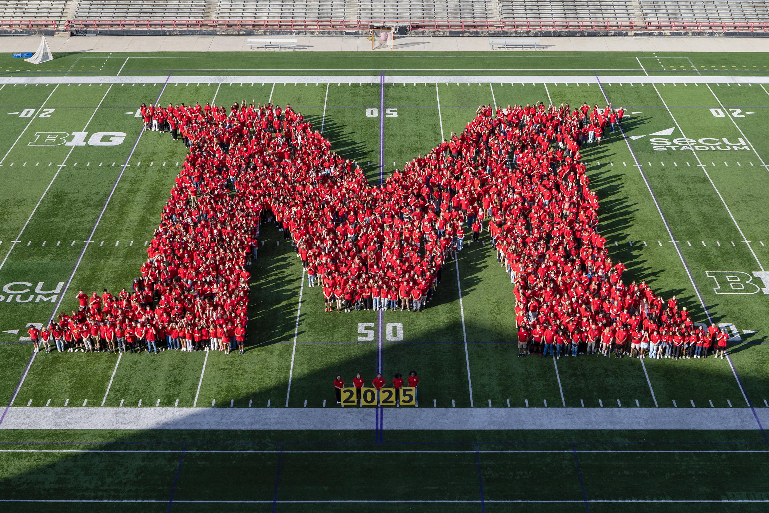 over 1,000 students wearing red shirts gathered in an M shape on the football field for a class photo