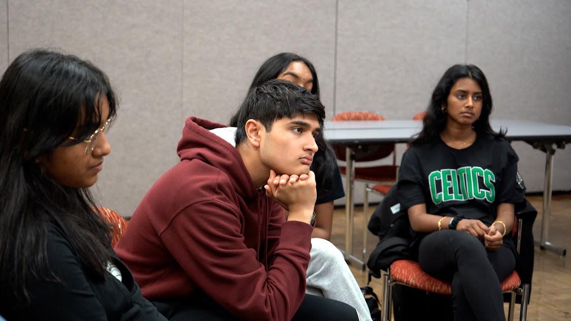 Four students seated indoors, listening attentively during a group discussion.
