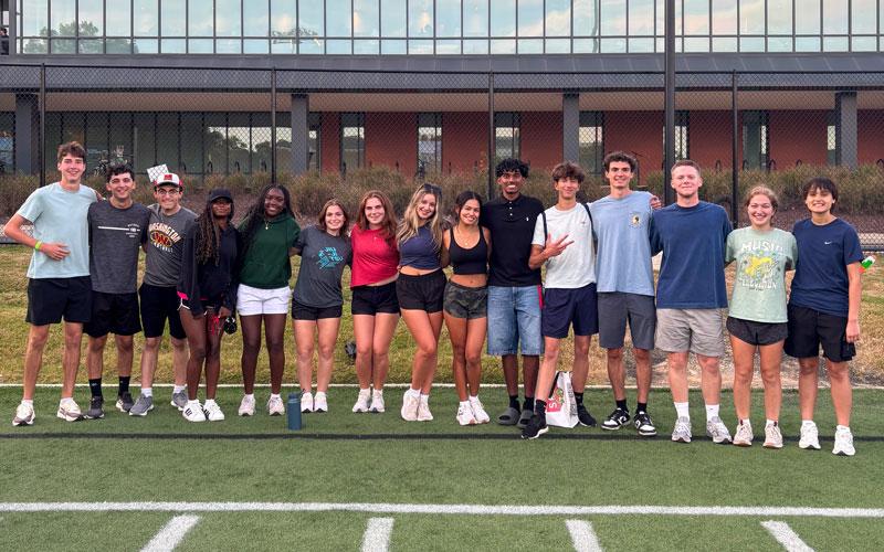 A large group of students posing together on a green turf field.