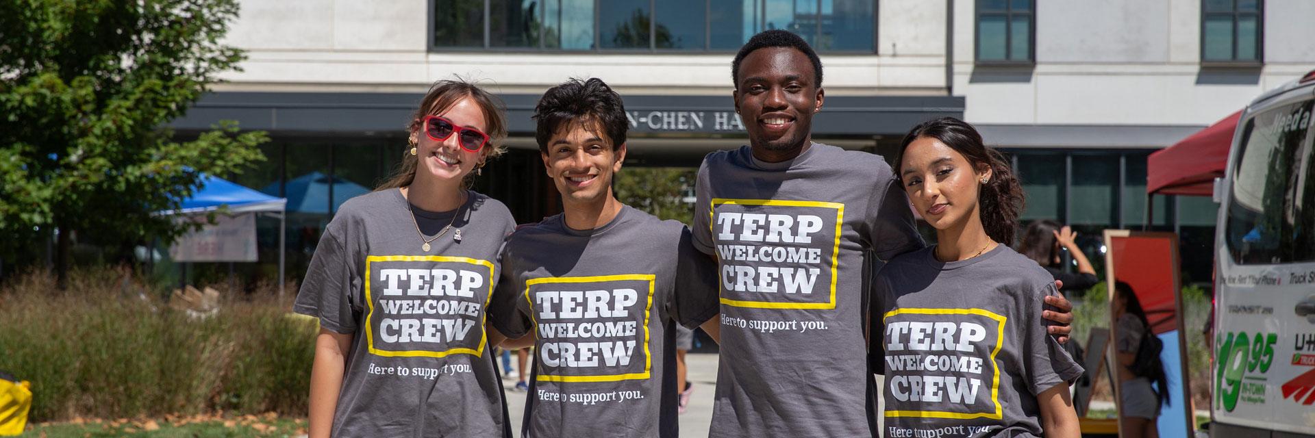 Four smiling student volunteers in Terp Welcome Crew shirts in front of Pyon-Chen Hall.