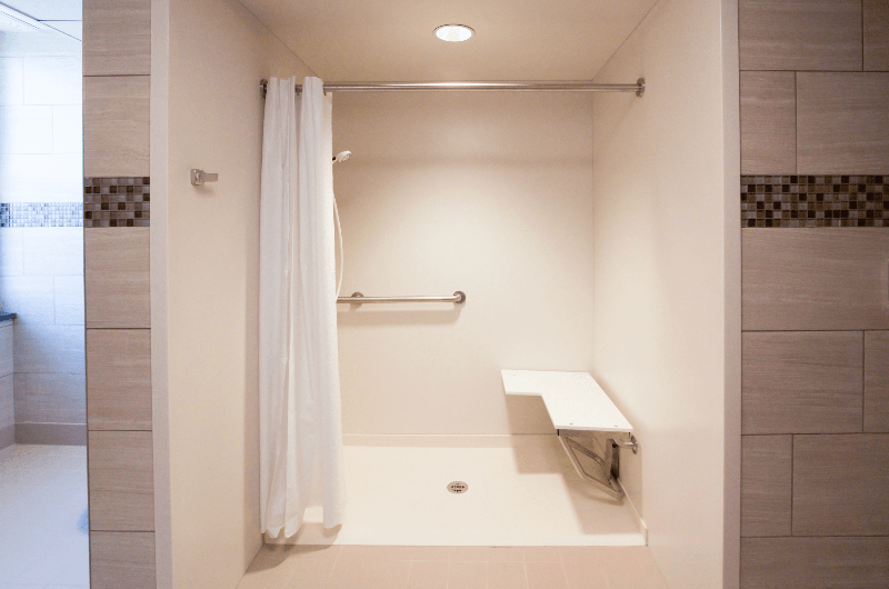 Accessible walk-in shower with a white curtain, safety grab bar, and a built-in folding bench.