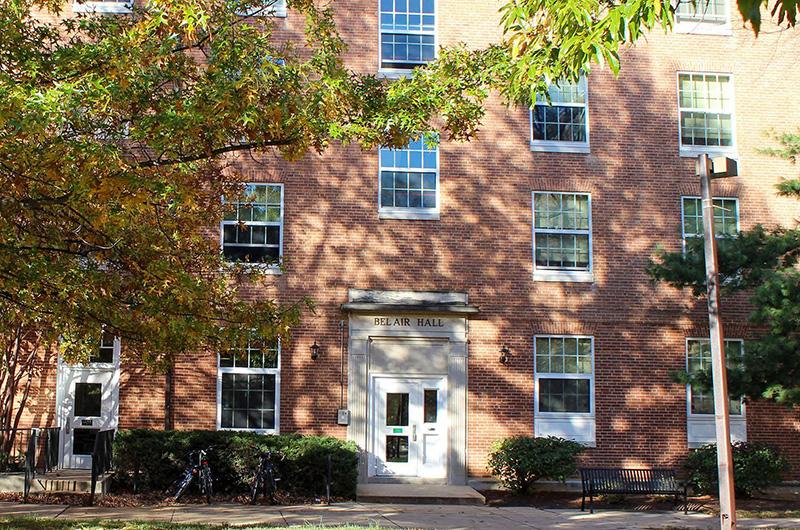 Exterior of brick Bel Air Hall with white door frame and autumn trees in the foreground.