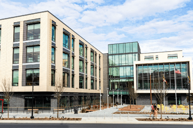 Modern and glass multi-story College Park City Hall building under a blue, cloudy sky.