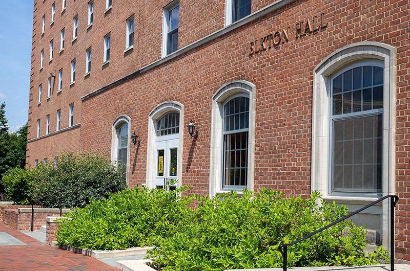 Exterior of brick Elkton Hall with arched white windows and green bushes in the foreground.