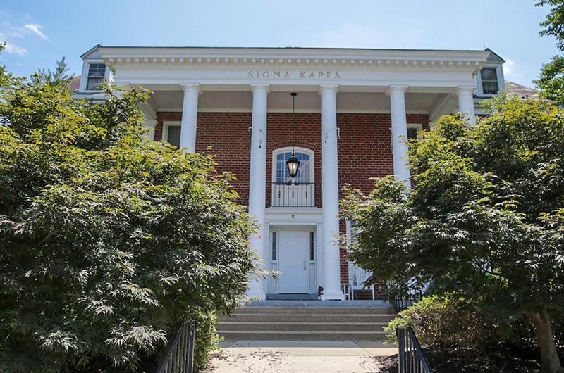Exterior of brick Sigma Kappa house with four white pillars and a small balcony.