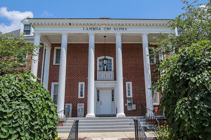 Exterior of brick Lambda Chi Alpha house with four white pillars and a small balcony.