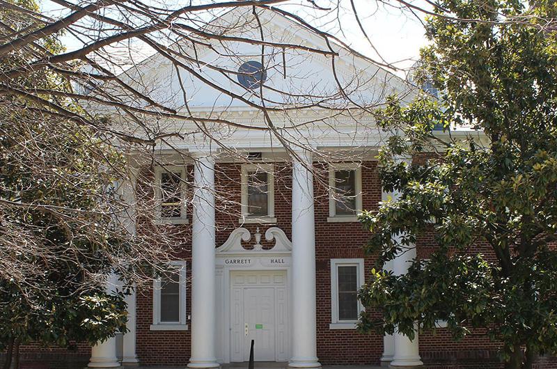 Exterior of Garrett Hall, a brick building with white pillars framed by large, leafy trees.