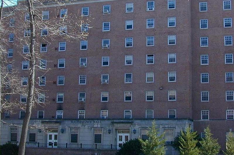Exterior of brick Hagerstown Hall with stone entryways and small green trees in the foreground.