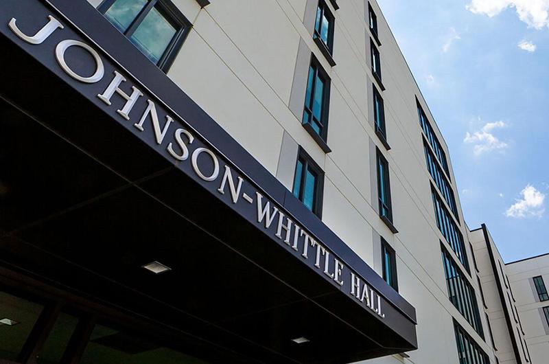 Low angle of modern white Johnson-Whittle Hall with large sign above glass entrance.