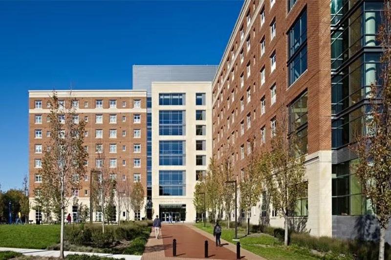 Exterior of large modern brick and stone Oakland Hall with a paved walkway and clear blue sky.