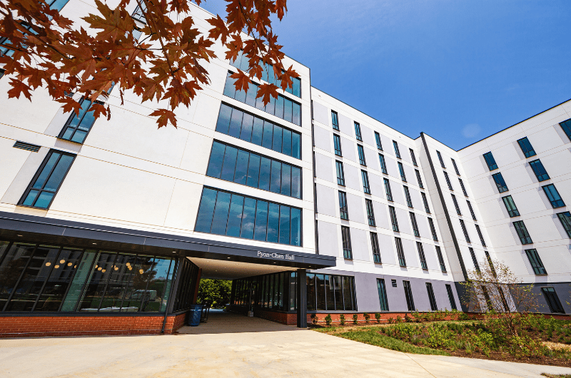Modern, multi-story Pyon-Chen Hall with white siding, large windows, and autumn leaves in foreground.