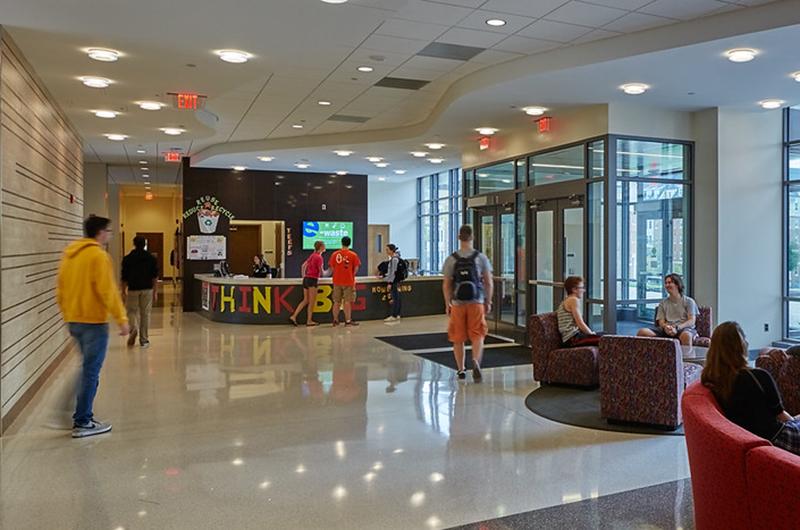 Modern residence hall lobby with a service desk, seating area, and large glass windows.